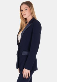 Blazer navy con un design elegante, rever in satin, due tasche frontali e una vestibilità su misura. Tessuto dalla trama liscia, silhouette strutturata.
