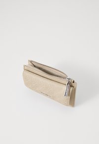 Beige lommebok med et teksturert mønster, som har to rom med glidelås og sølvfarget maskinvare. Kompakt design med en jevn overflate.