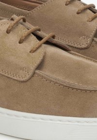 Brązowe zamszowe buty o gładkiej fakturze, z brązowymi sznurówkami, niskim fasonem i białą gumową podeszwą.