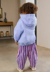 Felpa con cappuccio blu chiaro dal fit oversize, abbinata a pantaloni larghi a righe rosa e viola e scarpe beige glitterate.
