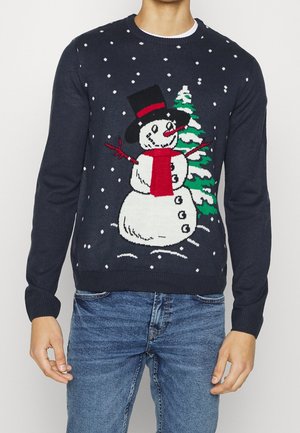 Maglione blu navy con un pupazzo di neve sorridente con cappello a cilindro nero, sciarpa rossa, braccia a forma di rami rossi, accanto a un pino coperto di neve con fiocchi di neve che cadono.