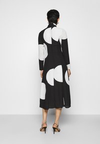 Schwarz-weißes Kleid mit langen Ärmeln und kreisförmigen Mustern. Entworfen mit einem taillierten Oberteil und ausgestelltem Rock, ausgestattet mit einem hohen Kragen.