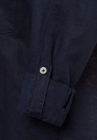 Camicia a maniche lunghe in lino blu scuro con polsino a bottoni, dotata di un bottone chiaro e di un tessuto liscio e strutturato.
