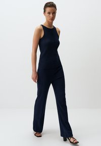 Top maniche scoperte in maglia a coste color navy abbinato a pantaloni a campana con design pulito e una trama sottile. Sandali neri con tacco completano l'outfit.
