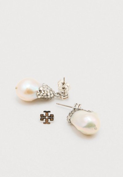 Μαργαριταρένια σκουλαρίκια με ασημένιες λεπτομέρειες, που διαθέτουν υφή κοντά στην καρφίτσα και μια μικρή μαύρη λεπτομέρεια σταυρού. Λείος, ιριδίζων επιφάνεια.