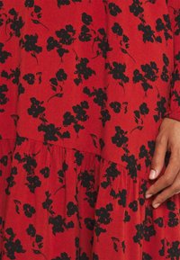 Vestido rojo con estampado de flores negras, con dobladillo plisado, tejido suave y mangas largas con puños elásticos.