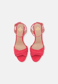 Červené semišové sandály s otevřenou špičkou, překříženými pásky a spona na kotníku, z pohledu shora na bílém pozadí.