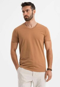 T-shirt marrone a maniche corte con scollatura a V; realizzato in tessuto morbido, presenta una vestibilità slim e una superficie liscia. Nessun motivo o logo visibile.