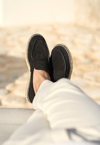 Schwarze Wildleder-Slipper mit einer gewebten Jute-Sohle und abgesteppten Details. Das Design zeichnet sich durch eine geschlossene Spitze und eine glatte Oberflächenstruktur aus.