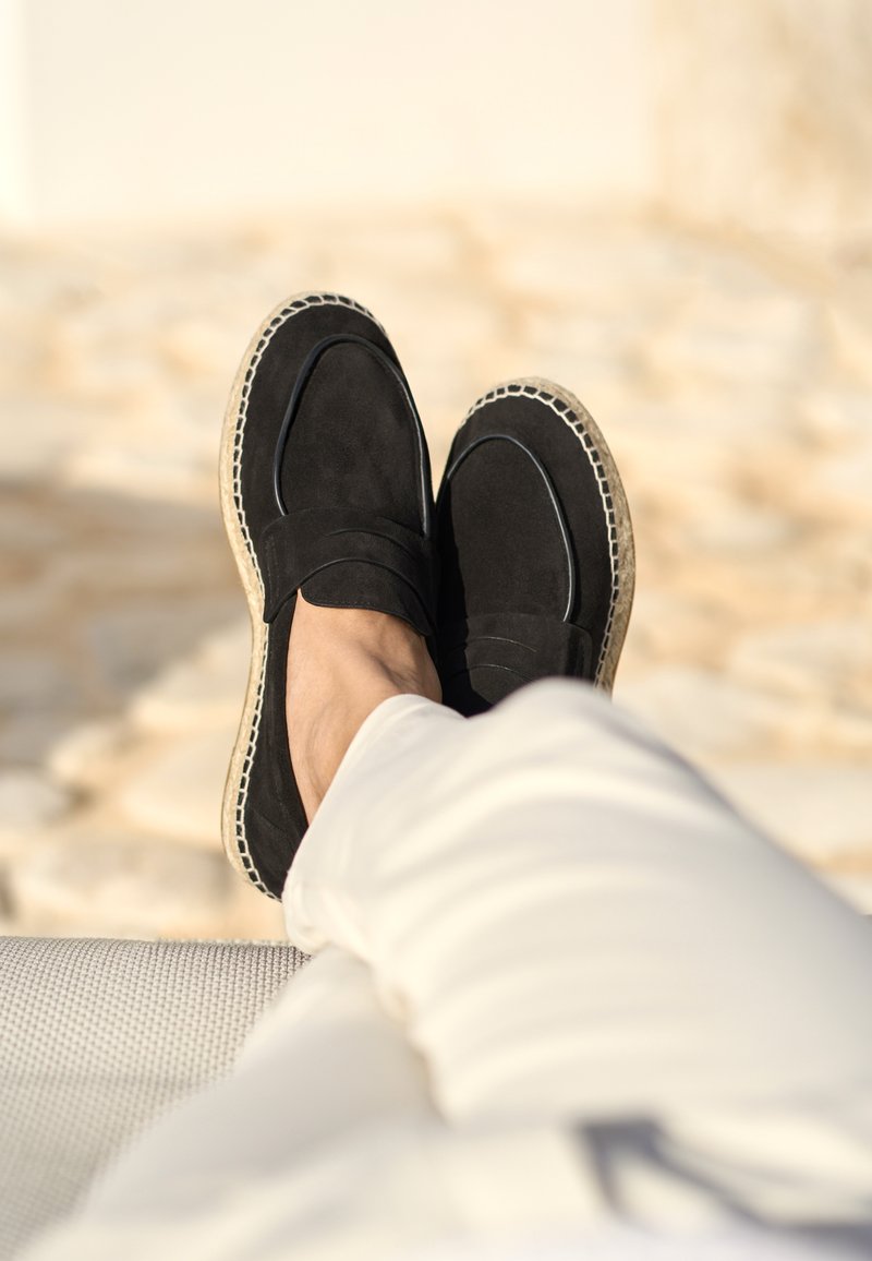 Schwarze Wildleder-Slipper mit einer gewebten Jute-Sohle und abgesteppten Details. Das Design zeichnet sich durch eine geschlossene Spitze und eine glatte Oberflächenstruktur aus.