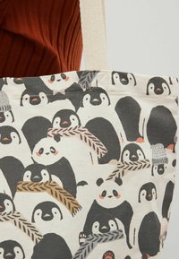 Et nærbillede af en tote bag med et fantasifuldt pingvin-design, hvor flere pingviner bærer hatte og holder på tørklæder.