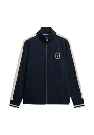 Navy zip-up jacket with cream side stripes and ribbed cuffs. Features a logo on the chest and two front pockets. Soft fabric texture.
