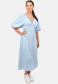 Robe bleu clair, longueur genou, en tissu texturé, avec un décolleté en V et des manches bouffantes. Portée avec des baskets blanches.