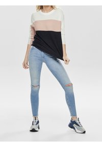 Sweter w kolorze kremowym, jasnoróżowym i czarnym w blokach kolorowych; połączony z jasnoniebieskimi, przetartymi skinny jeansami i wielokolorowymi butami sportowymi.