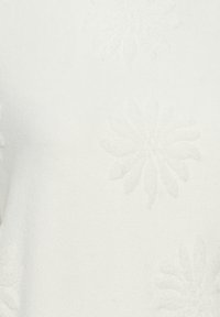 Bílé pletené svetřík s reliéfními květinovými vzory. Měkká textura s jemným leskem. Kolo výstřih a žádné viditelné zapínání.