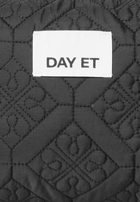 Svart quiltad tyg med ett geometriskt mönster, med en vit etikett som visar texten "DAY ET" fäst.