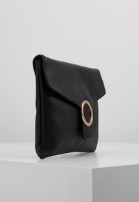 Svart läderkuvert med en kuvertdesign, som har en guldcirkel som accent på framsidan och en slät, matt textur.