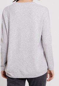 Pull gris à manches longues, ourlet arrondi et texture douce. Caractérisé par une coupe décontractée et un design simple et minimaliste.