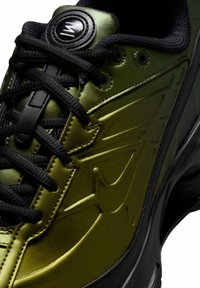 Scarpa da ginnastica verde e nera con lacci neri, pannello laterale strutturato e logo circolare sulla linguetta imbottita.