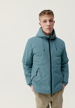 Chaqueta impermeable de color azul claro con capucha, cremallera frontal y puños elásticos. Presenta dos bolsillos laterales con cremallera y una textura suave.