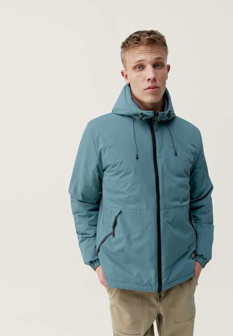 Svetloplava vodoodporna jakna s kapuco, sprednjim zadrgo in elastičnimi manšetami. Ima dve stranski žep z zadrgo in gladko teksturo.