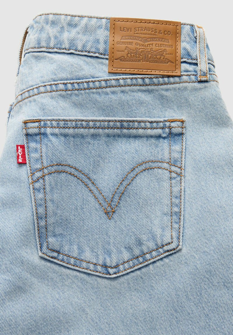 Light blue denim jeans featuring a leather tag with embossed details. Distinct back pocket stitching forms a double arc design. Red Levi’s tab visible.