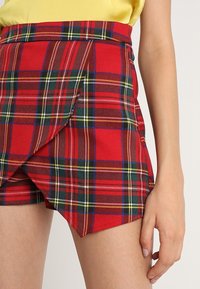 Rode geruite korte broek met een wikkelontwerp en groene en gele accenten. De stof heeft een gladde textuur en een aansluitende taille.