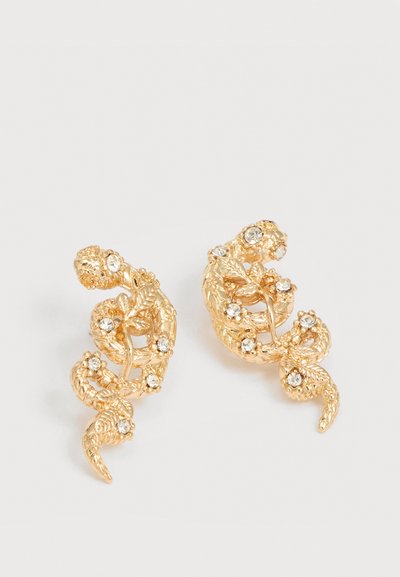 Σκουλαρίκια σε χρυσαφί απόχρωση, σχηματισμένα σαν τυλιγμένα φίδια με υφή φύλλων και ενσωματωμένες διαυγείς στρας σε λευκό φόντο.