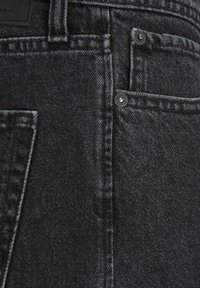 Černé džíny z denimu s klasickým designem pěti kapes, viditelným šitím a kovovými zapínáními se strukturovaným povrchem.