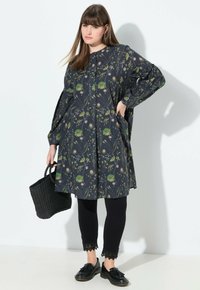 Blumenmusterkleid mit dunklem Hintergrund, langärmlig und locker geschnitten. Kombiniert mit schwarzen Leggings und einer strukturierten Handtasche.