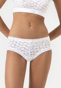 Witte kant onderbroek met hartpatronen, gegolfde randen en een zachte tailleband. De stof heeft een doorschijnende, gestructureerde uitstraling.