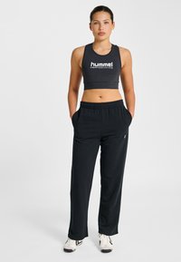 Svart sport-BH med "hummel PERFORMANCE"-logotyp, kombinerad med lösa svarta sweatpants med sidofickor, avslutad med vita sneakers.