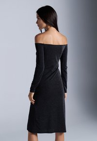 Robe noire décolletée, à manches longues, avec une silhouette ajustée et un subtil éclat. Le tissu est lisse et a une longueur mi-mollet.