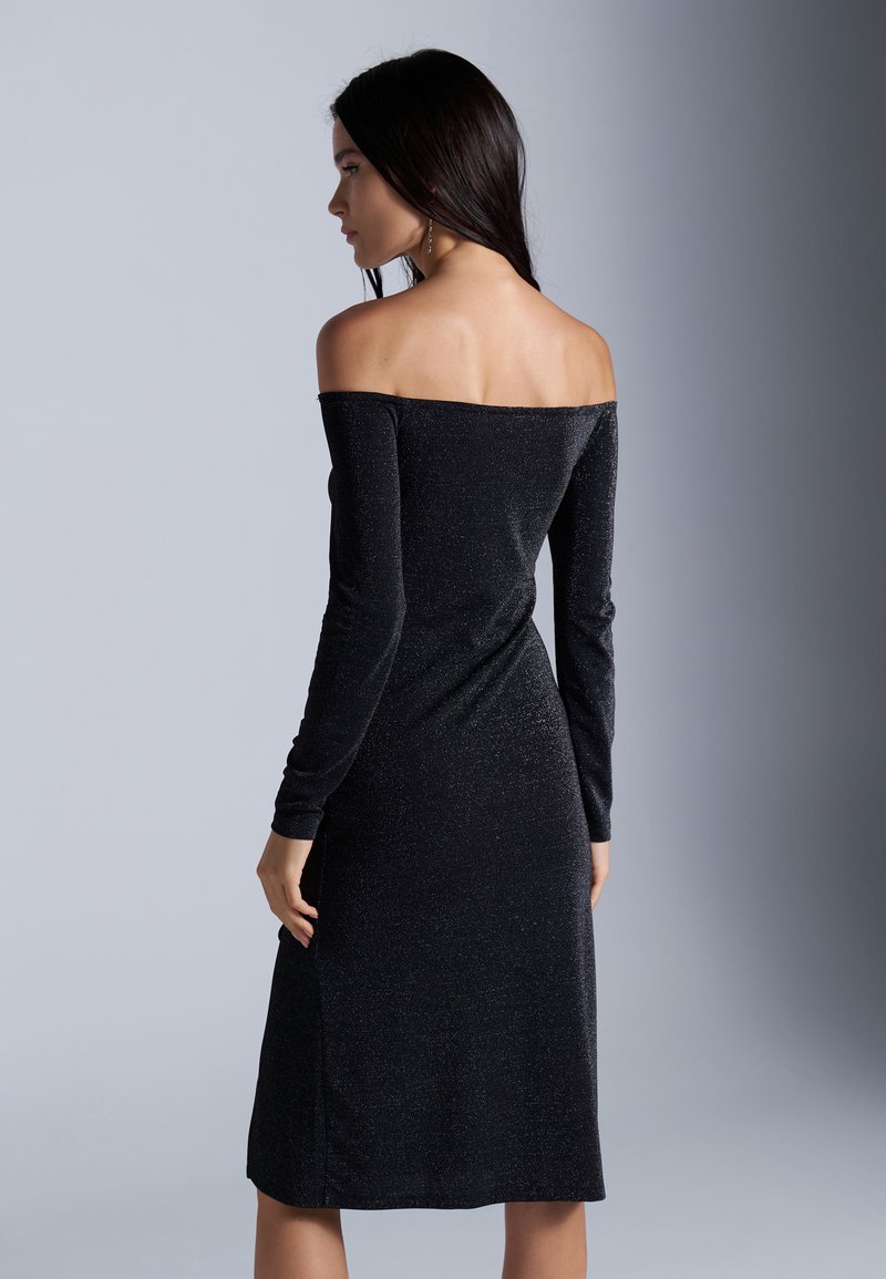 Robe noire décolletée, à manches longues, avec une silhouette ajustée et un subtil éclat. Le tissu est lisse et a une longueur mi-mollet.