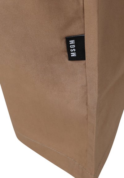 Borsa di stoffa marrone con una texture opaca, caratterizzata da un'etichetta nera con scritte bianche. Design semplice e strutturato con linee pulite.