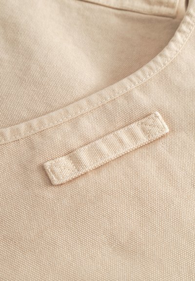 Zbliżenie na beżową, teksturowaną tkaninę z przeszytym pętelkowym detalem i zakrzywionym szwem.
