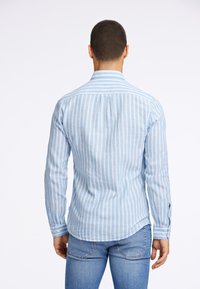 Jasnoniebieska koszula w paski z długimi rękawami, mankietami na guziki i zakładką z tyłu. Połączona z jasnoniebieskimi dżinsami, tworząc spójną całość.