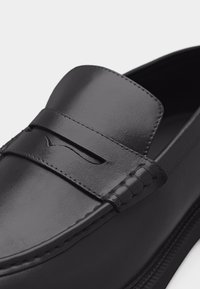 Mocassin en cuir noir avec une bride à coque et des coutures détaillées le long du cou-de-pied et des côtés.