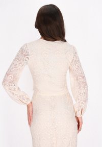 Abito in pizzo crema a maniche lunghe con intricate fantasie floreali, vita aderente e maniche soffici a sbuffo con dettagli di bottoni.
