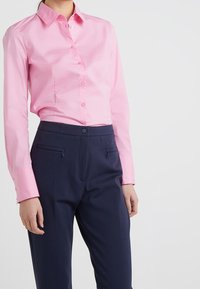 Camicia button-up rosa chiaro con maniche lunghe, dotata di colletto. Abbinata a pantaloni su misura blu navy scuri con tasche frontali con zip.