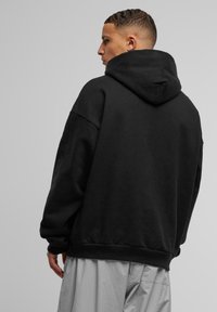 Zwarte oversized hoodie met een zachte textuur en een grote, verstelbare capuchon. Heeft verlaagde schouders en een geribbelde onderzoom voor een ontspannen pasvorm.