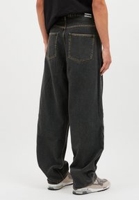 Tummanharmaat ylisuuret farkut, joissa on korkea vyötärö, mukana kaksi takataskua ja näkyvät ompeleet, yhdistettynä vaalenvärisiin tennareihin.