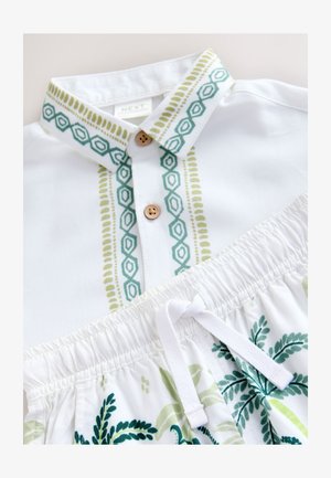 Bela srajca z zeleno in modro-zeleno geometrijsko vezenino ob ovratniku in obroču ter kratke hlače z zategovalnim trakom in cvetličnim vzorcem.