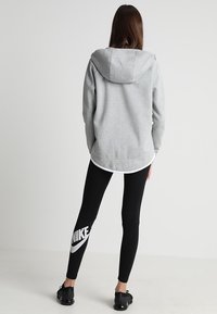 Grå hooded sweatshirt med lös passform, ihopparad med svarta leggings med en vit Nike-logotyp. Slät textur, avslappnad design.