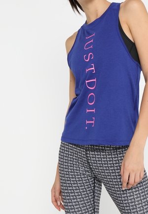 Femme portant un débardeur bleu avec le texte rose « JUST DO IT. » et des leggings noirs recouverts d'un motif répétitif « Just do it. ».