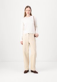 Maglione beige chiaro, colletto a girocollo, tessuto morbido; abbinato a pantaloni crema a vestibilità comoda con pieghe frontali. Scarpe con tacco marroni, design minimalista.