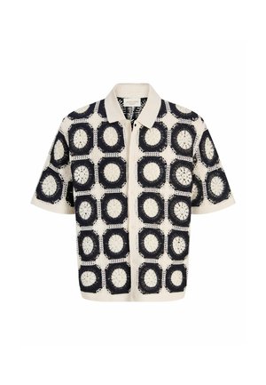 Camisa de manga corta con cuello, con cuadrados de ganchillo en negro y crema que presentan patrones florales circulares y cierre frontal con botones.