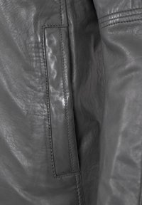 Gray leather jacket with a smooth texture, featuring a side pocket and visible stitching. The material appears soft and slightly shiny.