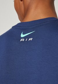 Tmavě modré tričko s kulatým výstřihem, na zádech je světle modré logo Nike swoosh a nápis "AIR". Měkká bavlněná tkanina.