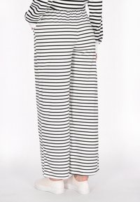 Pantaloni larghi a righe nere e bianche, con vita elastica e una morbida texture del tessuto. Abbinati a scarpe bianche.
